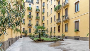 A courtyard with yellow buildings, potted plants, and a tiled floor. - Appartamento Puccini - La Vista Apartments (Milan)