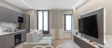Une cuisine moderne dotée d’un four et d’un micro-ondes encastrés, un coin repas avec une table préparée pour deux personnes, et un grand téléviseur à écran plat fixé au mur.