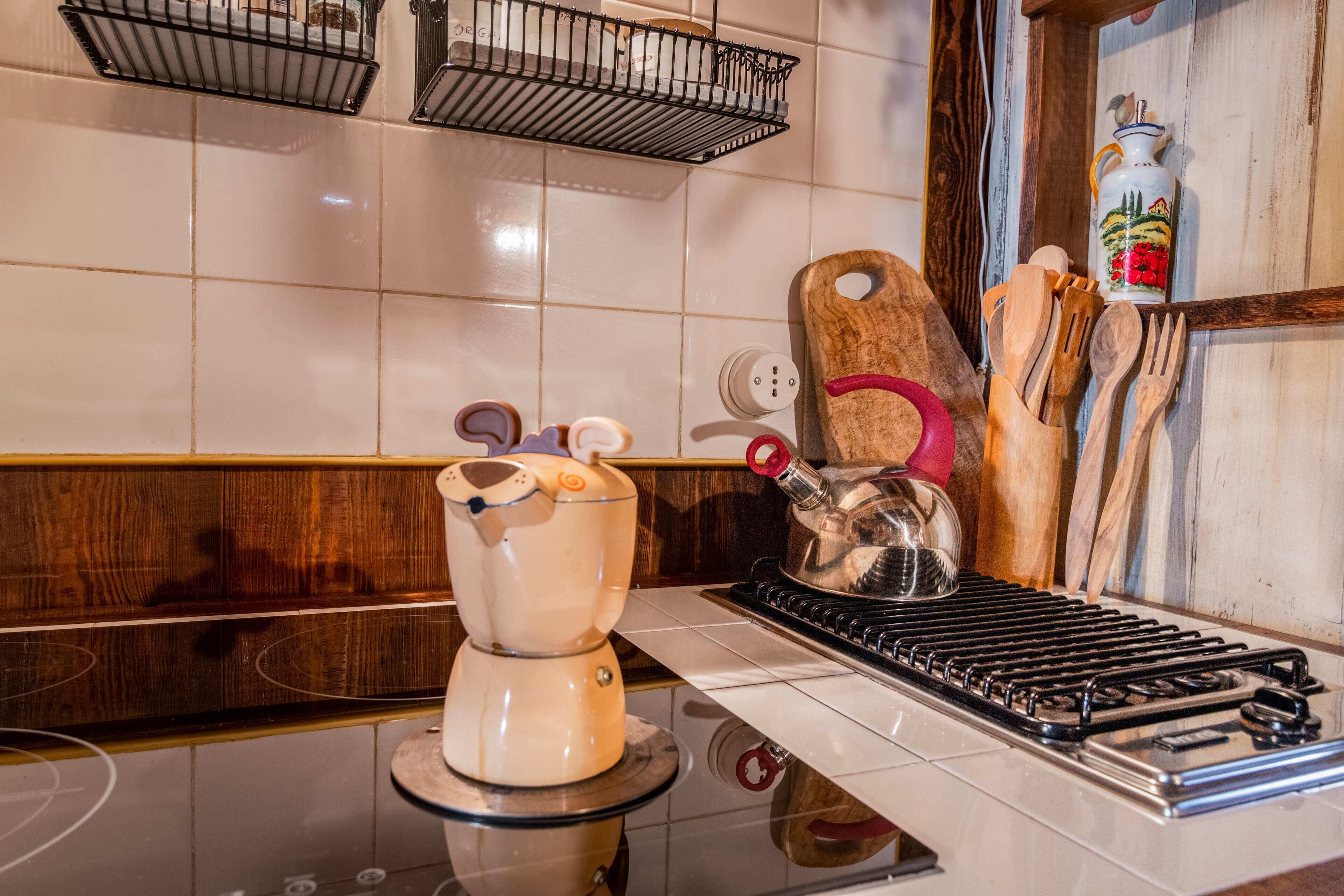 A kitchen with a stove, a kettle, and wooden utensils on the counter.