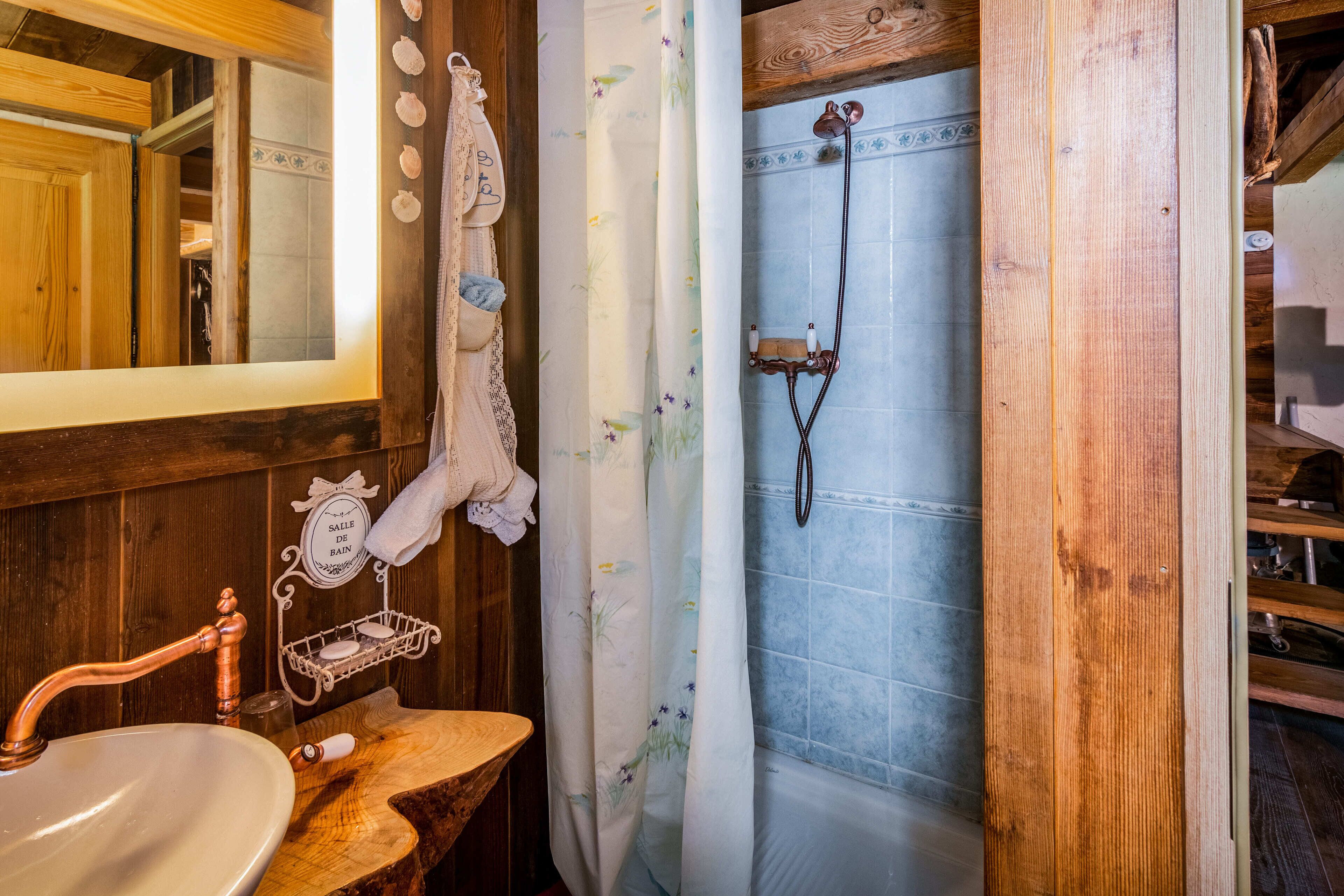 Een badkamer met een houten wastafelmeubel, een koperen kraan, een douche met een houten deur en een handdoekhouder met handdoeken.
