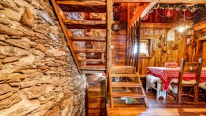 Un intérieur rustique avec un mur en pierre, un escalier en bois et un coin repas agrémenté d’une nappe rouge.