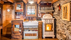 Une cuisine rustique avec un mur en pierre, des poutres en bois, un poêle blanc et une fenêtre ornée de rideaux à carreaux.