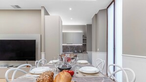 Un espace repas moderne avec une table en marbre, des chaises blanches et un grand téléviseur à écran plat.