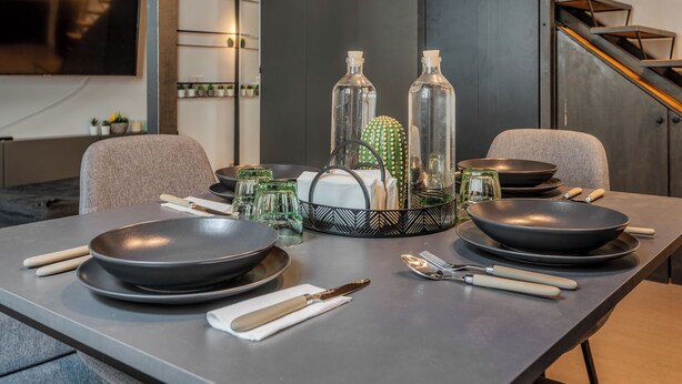 A modern dining table set with black plates, cutlery, and glassware, surrounded by decorative items like a cactus and glass bottles. - Loftino Bocconi - La Vista Apartments (Milano)