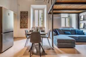Eine moderne Küche mit einem Edelstahl-Kühlschrank, einem Esstisch mit Stühlen und einem blauen Sofa im Wohnbereich.