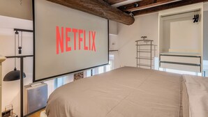 A bedroom with a large bed, a wall-mounted TV displaying the Netflix logo, a wardrobe, and a metal shelf unit. - Loftino Bocconi - La Vista Apartments (Milano)
