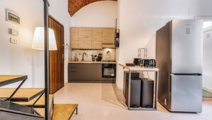 A modern kitchen with a stainless steel refrigerator, a built-in oven, and a sink. There is a wooden cabinet above the sink and a small table with a lamp. - Loftino Bocconi - La Vista Apartments (Milano)