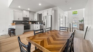 Una cocina moderna con armarios blancos, una isla central y un comedor con una mesa y sillas de madera en patrón de espiga.