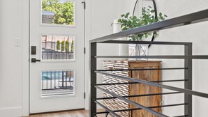 Una puerta blanca con tres ventanas, un estante metálico con listones de madera y una planta en maceta en la pared.