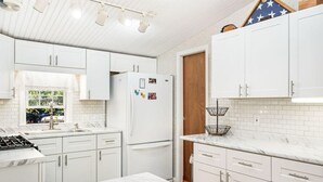 Een moderne keuken met witte kastjes, een marmeren aanrechtblad en een ingebouwde gasoven.