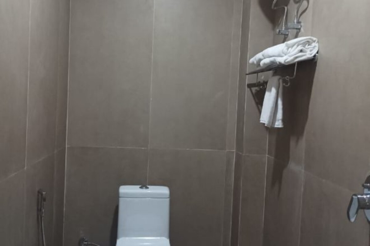 A bathroom with a toilet, a towel rack with a folded towel, and a showerhead.