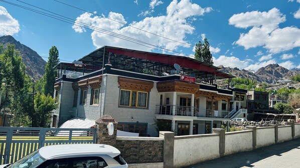 A hotel with a red roof, multiple balconies, and a view of mountains. - Hillside Homestay and Hostel (Leh)