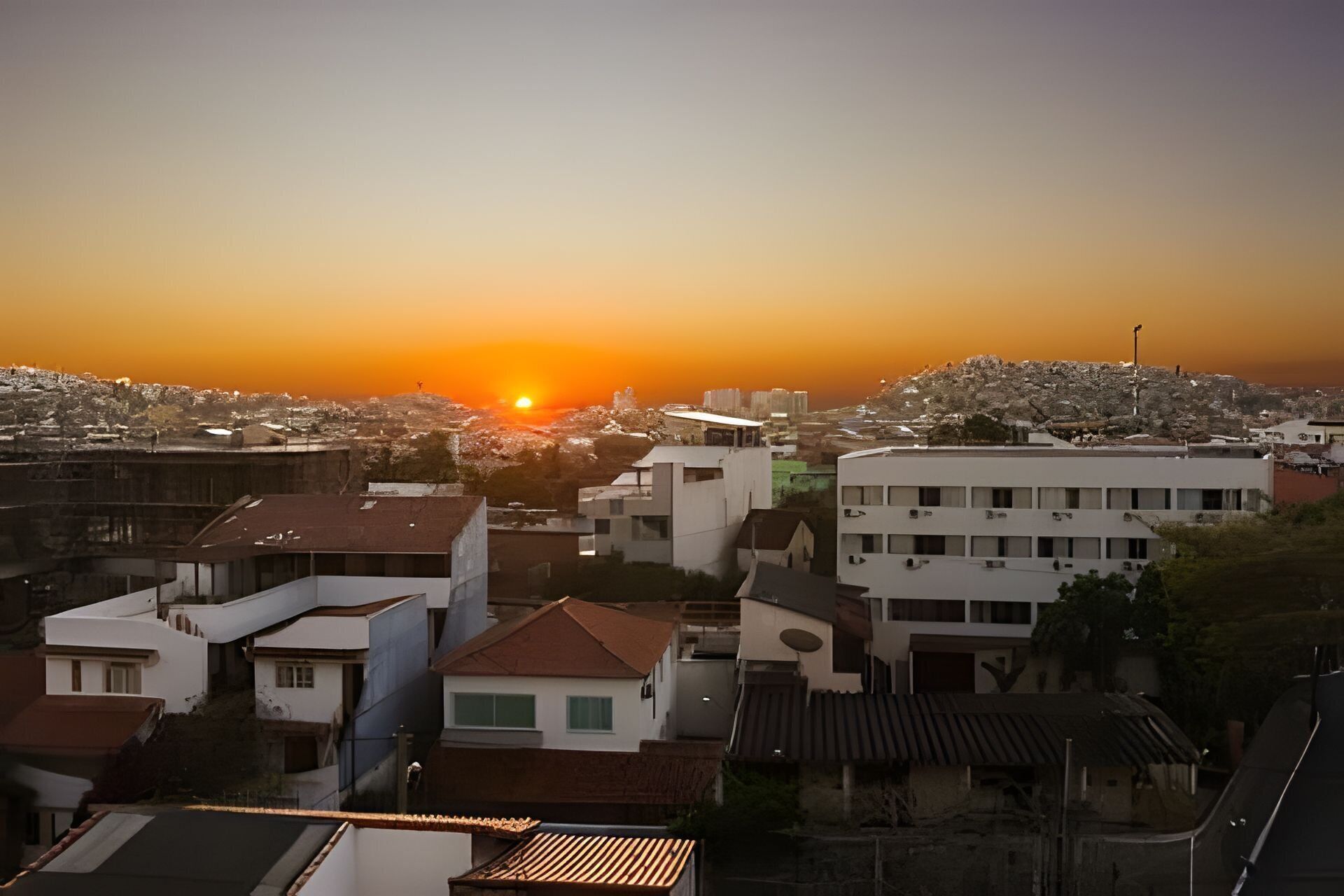 Paesaggio urbano al tramonto, con edifici e una collina sullo sfondo.