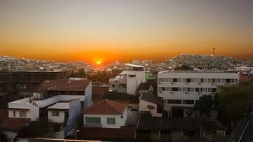 Paesaggio urbano al tramonto, con edifici e una collina sullo sfondo.