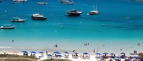 A beach with boats, umbrellas, and people.
