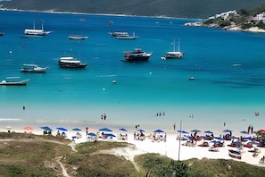 A beach with boats, umbrellas, and people. - Habitat Hospedagens (Arraial do Cabo)