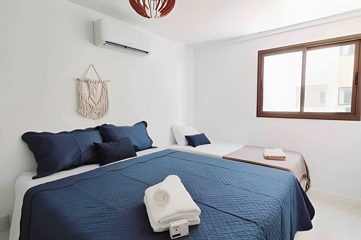 A bedroom with a bed, bedside tables, a window, and an air conditioning unit.