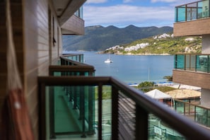 Un edificio moderno con balcón de cristal que da a una masa de agua y un paisaje montañoso.