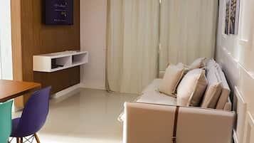 Une chambre moderne avec un canapé, une table, un téléviseur fixé au mur et une fenêtre avec des rideaux.