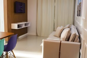 Une chambre moderne avec un canapé, une table, un téléviseur fixé au mur et une fenêtre avec des rideaux.