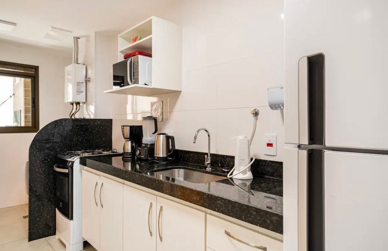 Une cuisine moderne équipée d’une cuisinière, d’un évier et d’un réfrigérateur, avec des meubles blancs et une fenêtre.