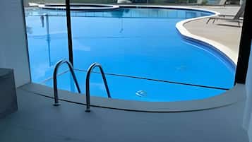Une piscine intérieure moderne avec des parois en verre transparent, un design incurvé et un escalier en métal.