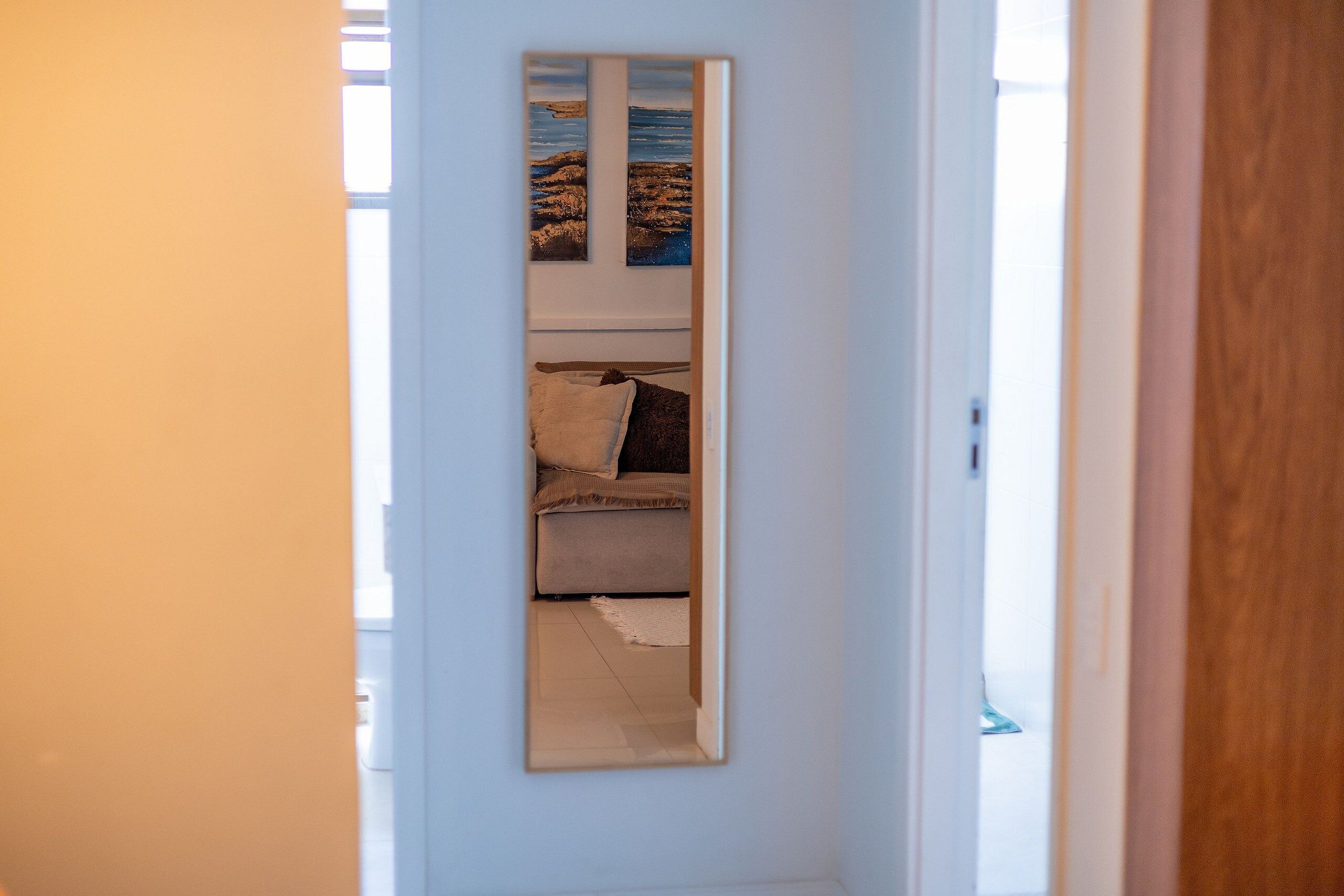 Een smalle gang met een bed en een spiegel die een kamer met een bed en een raam weerspiegelt.