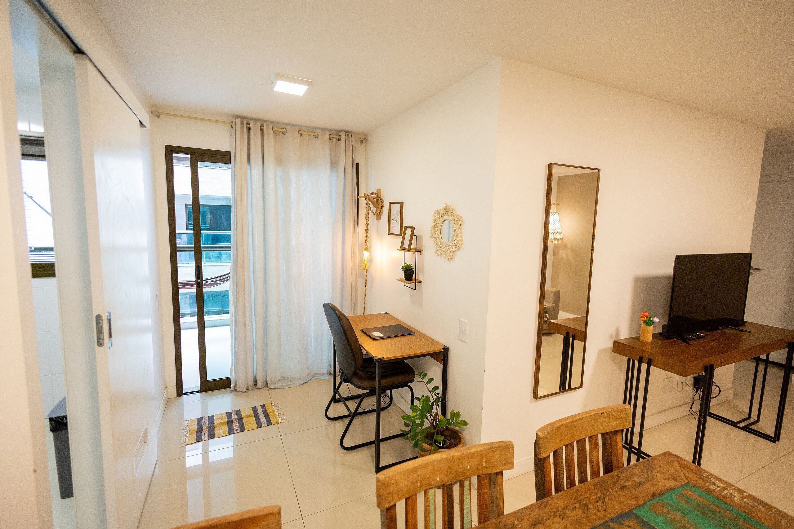 A modern living room with a wooden dining table, a sofa, a TV, and a large mirror.