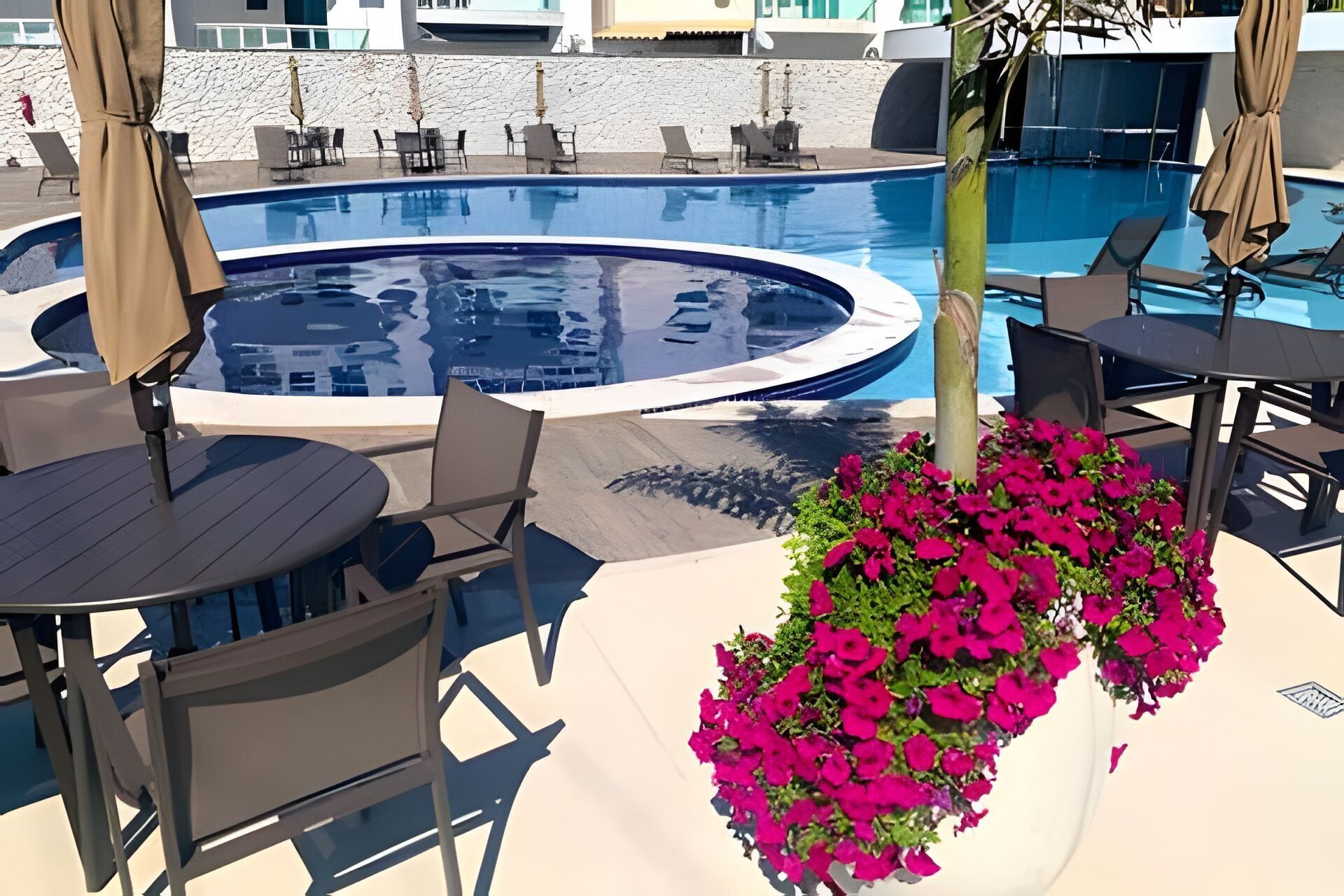 Un área de piscina con sillones reclinables, un jacuzzi y una jardinera con flores.