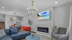 A modern living room with a sectional sofa, a grey armchair, a round coffee table, a fireplace, and a TV mounted on the wall.