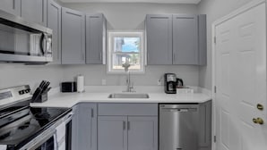 A modern kitchen with grey cabinets, a stainless steel dishwasher, and a coffee bar.