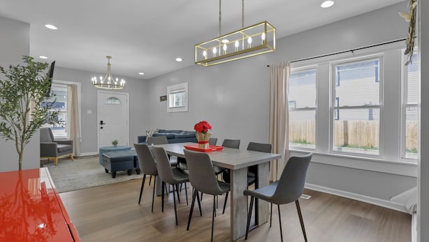 A modern dining area with a rectangular table, grey chairs, and a chandelier.