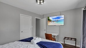 A hotel room with a bed, a desk, a chair, a TV, and a view of a beach.