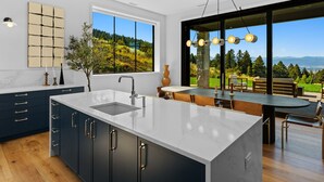 Eine moderne Küche mit einer großen Kochinsel, dunklen Schränken und Blick auf eine reizvolle Landschaft durch große Fenster.