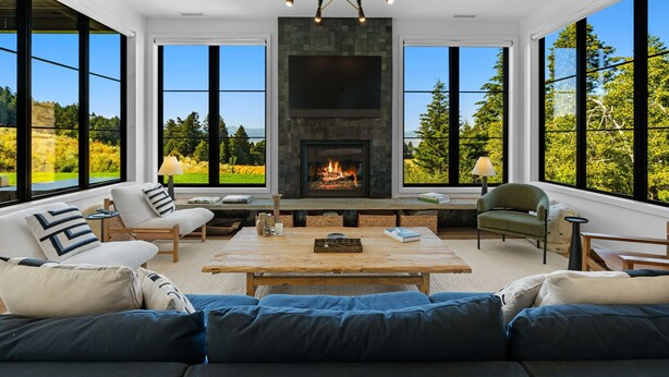 Ein modernes Wohnzimmer mit Kamin, großen Fenstern und Blick ins Freie.