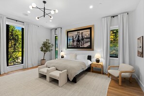 A modern bedroom with a large bed, two bedside tables with lamps, a chair, and a large window with curtains. - Resolute Ridge Meadow House (Bozeman)