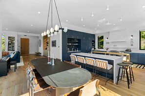 A modern kitchen with a central island, bar stools, and a dining area with a large table. - Resolute Ridge Meadow House (Bozeman)
