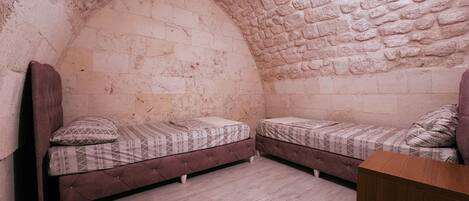 Una habitación con dos camas, un cabecero de madera, una pared de piedra y un armario de madera.