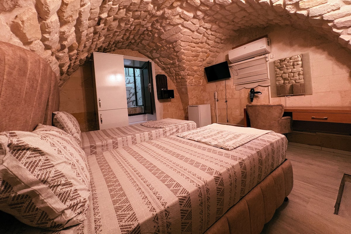 Un dormitorio con techo de piedra, una cama con ropa de cama estampada, un armario, un escritorio y un televisor montado en la pared.