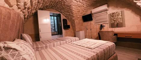 A bedroom with a stone ceiling, a bed with patterned bedding, a wardrobe, a desk, and a television mounted on the wall.