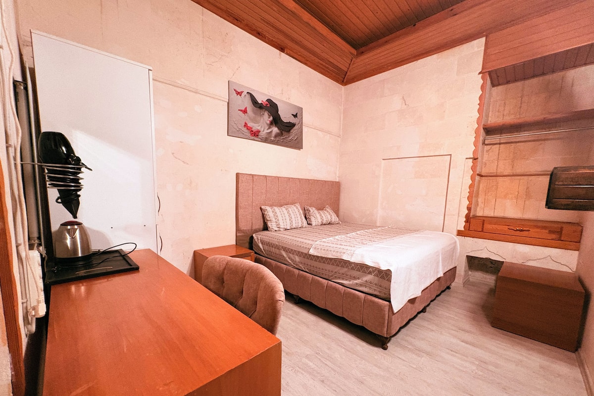 Un dormitorio con cama, escritorio y silla. Hay un cuadro en la pared y una ventana con contraventanas de madera.