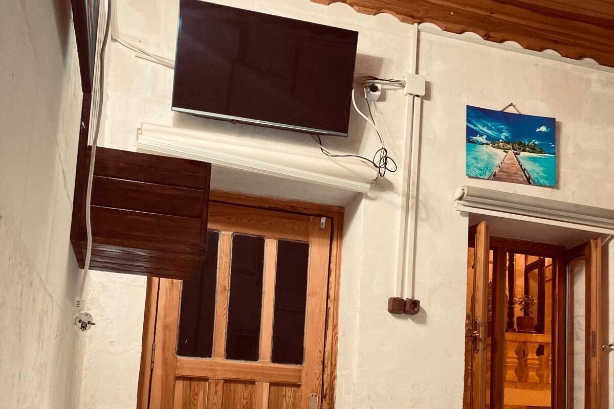 Una habitación con puerta de madera, un televisor montado en la pared y un cuadro de paisaje tropical.