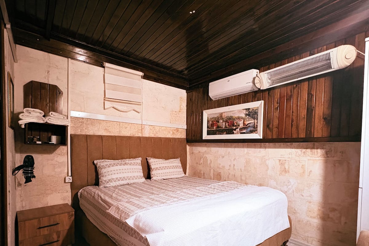 Un dormitorio con una cama de madera, una mesita de noche, una silla y un calentador de pared.
