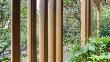 A view through wooden slats of a balcony with greenery and a road in the background.