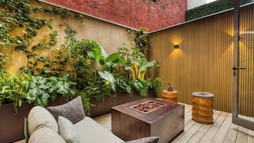 A cozy outdoor seating area with a cushioned sofa, a wooden coffee table, and a planter wall with various plants.
