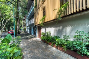 A narrow urban street with buildings on either side, a red car parked on the left, and a row of potted plants along the sidewalk. - Casa Tasman (Mexico City)