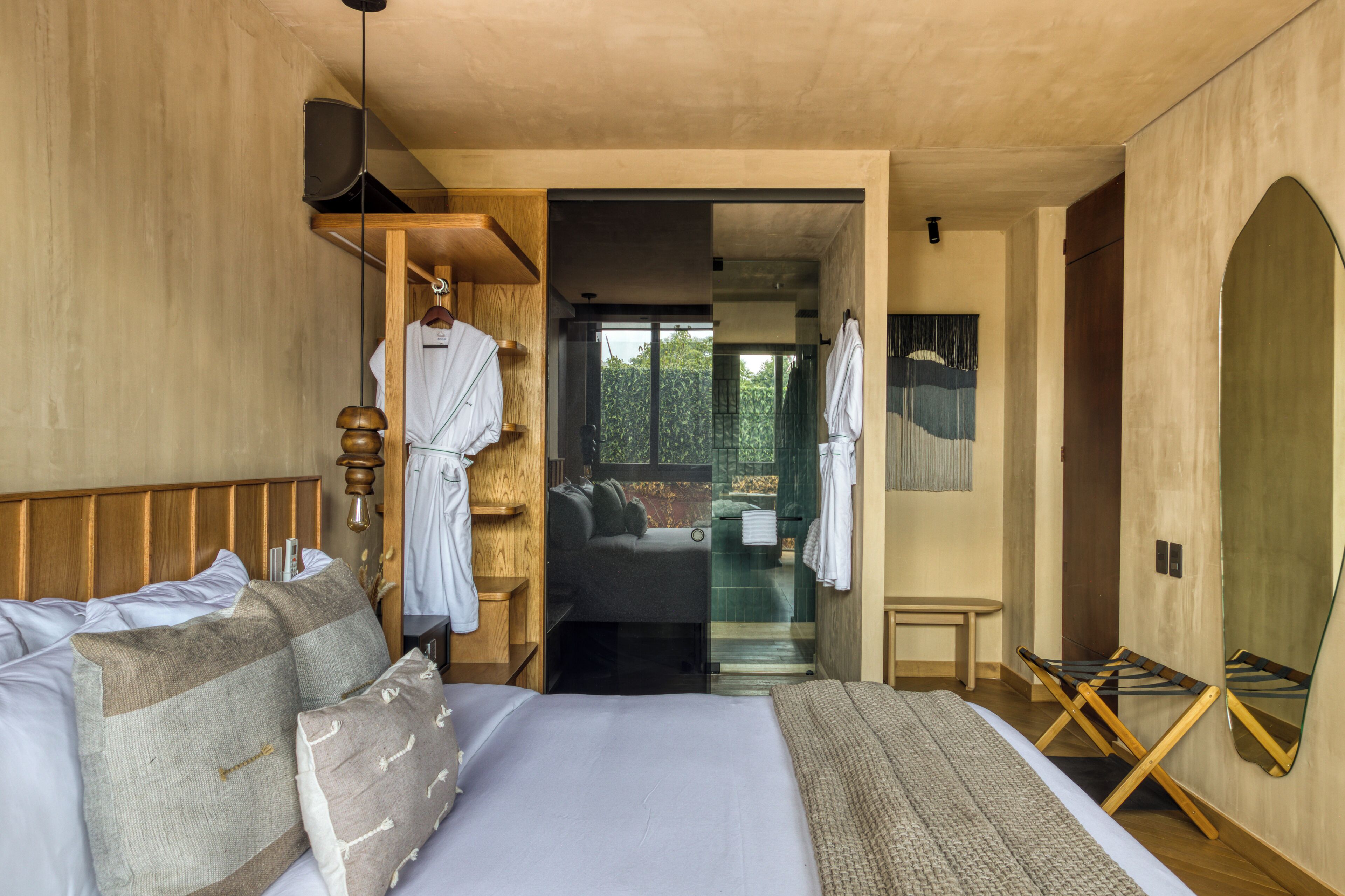 Un dormitorio con una cama grande, cabecera de madera, un perchero, una mesita pequeña y un banco.