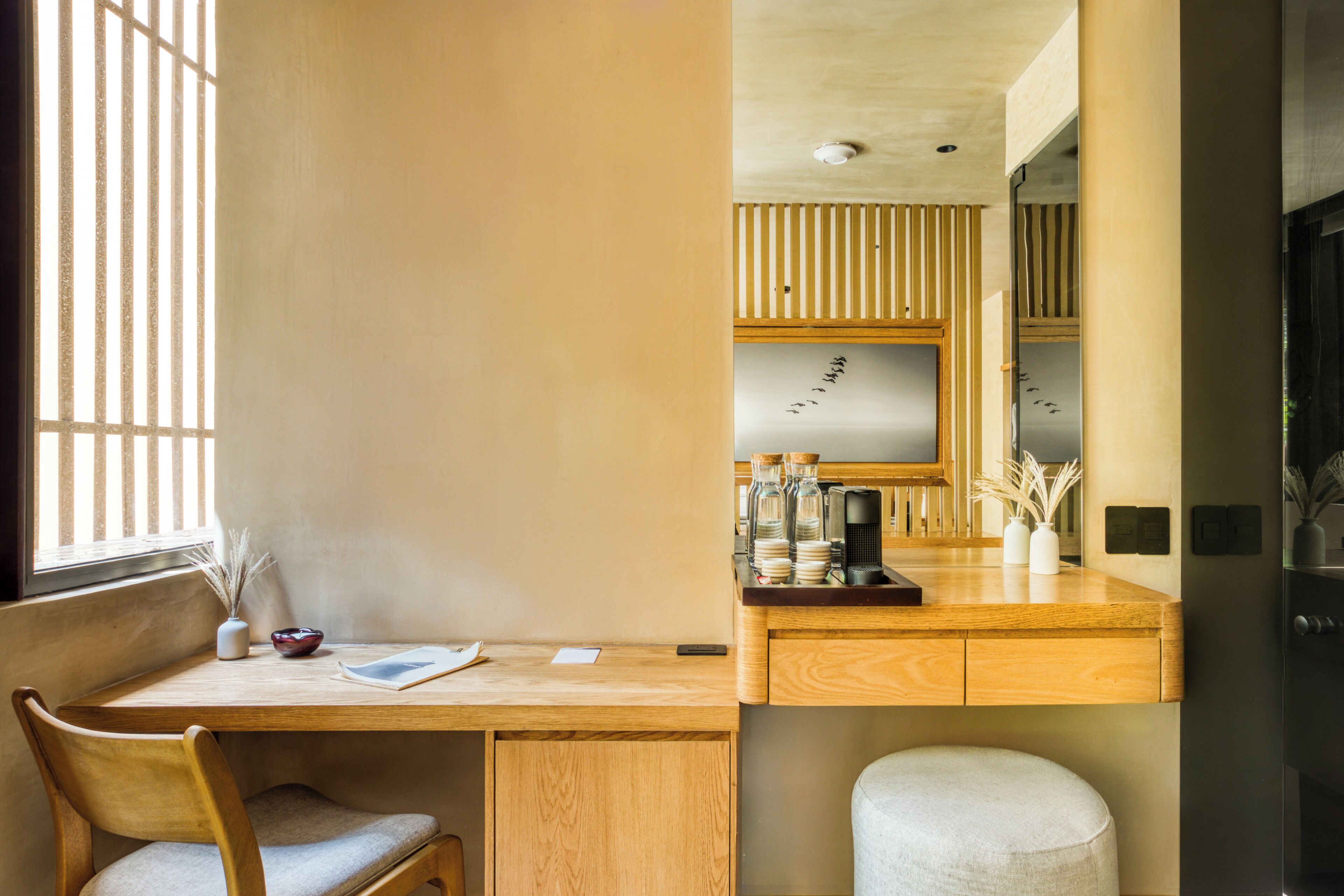 A modern room with a wooden desk, a chair, a small table, and a window with vertical blinds.