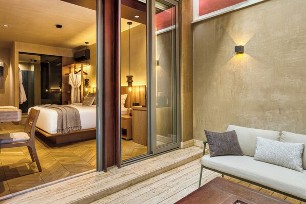 A modern hotel room with a bed, a sofa, a chair, a small table, and a glass door leading to a bathroom. - Casa Tasman (Mexico City)