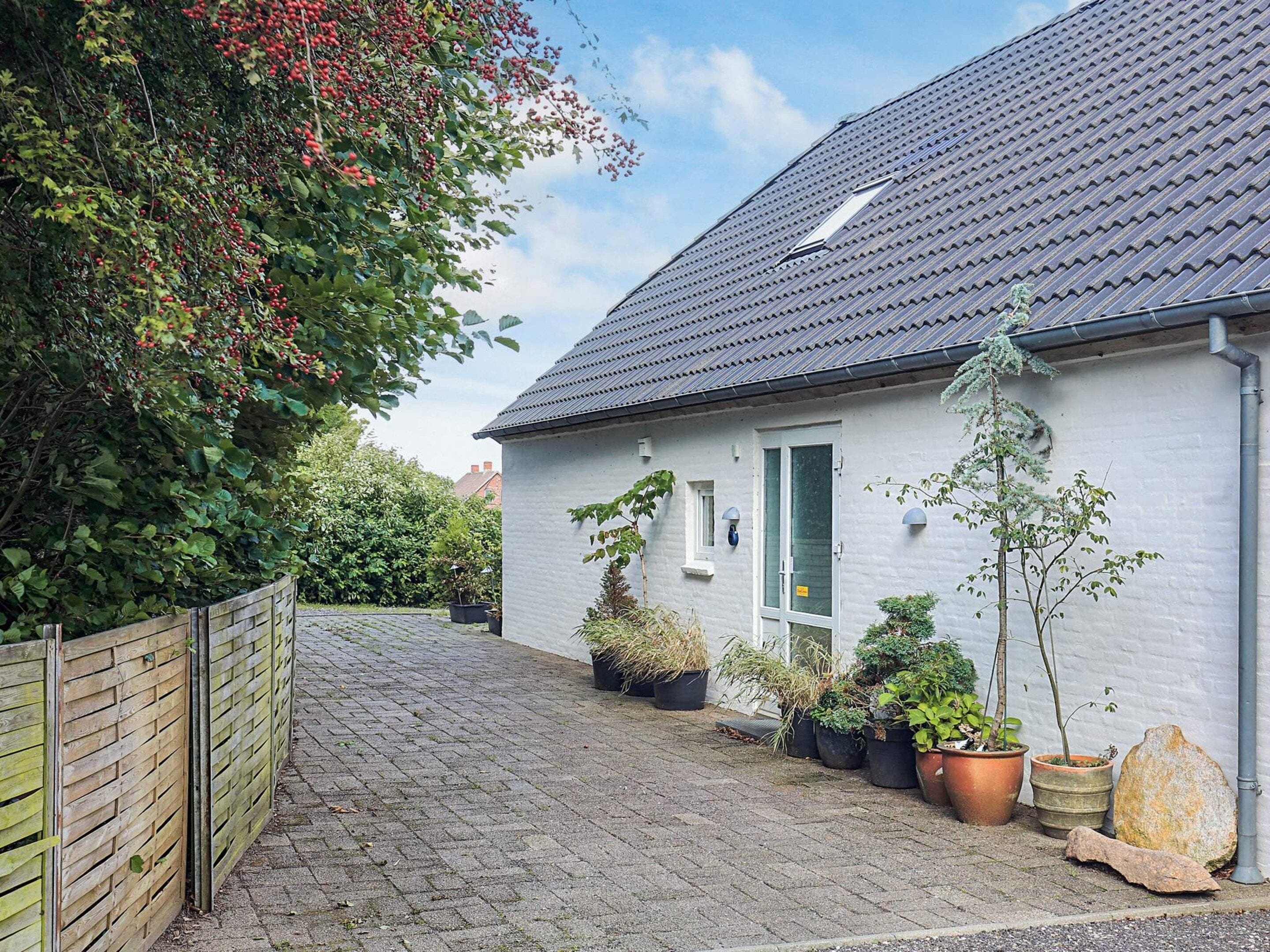 Une maison avec une allée pavée, une clôture en bois et des plantes en pot.